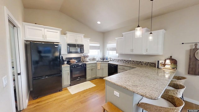 kitchen with black appliances, a peninsula, light wood-style floors, a sink, and a breakfast bar