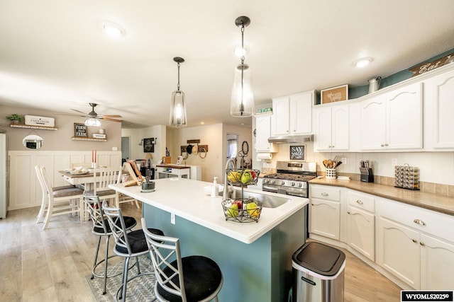 750 N Adams Ave, Buffalo, WY 82834 - kitchen with stainless steel gas range oven, under cabinet range hood, a ceiling fan, a kitchen breakfast bar, and white cabinetry