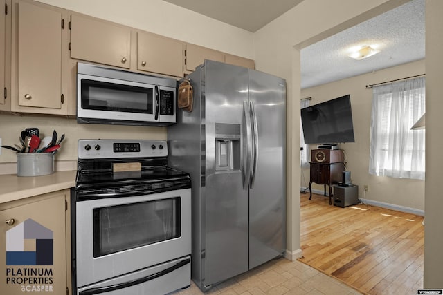 kitchen with stainless steel appliances, light countertops, baseboards, light wood-style flooring, and a textured ceiling