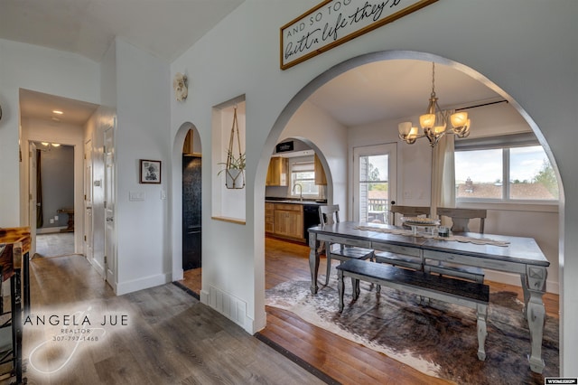 dining space featuring wood finished floors, a chandelier, arched walkways, vaulted ceiling, and baseboards