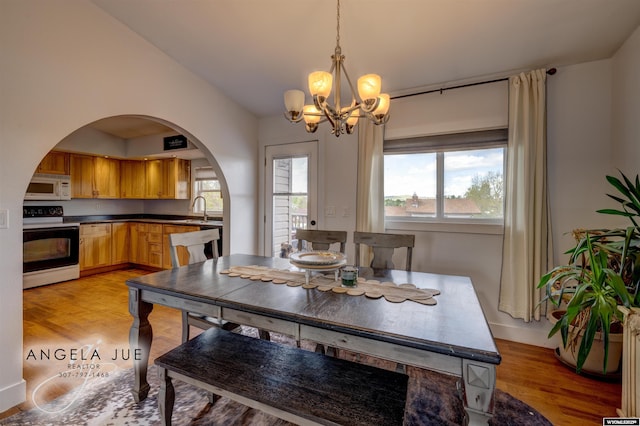 dining room featuring a chandelier, light wood-style flooring, arched walkways, lofted ceiling, and baseboards
