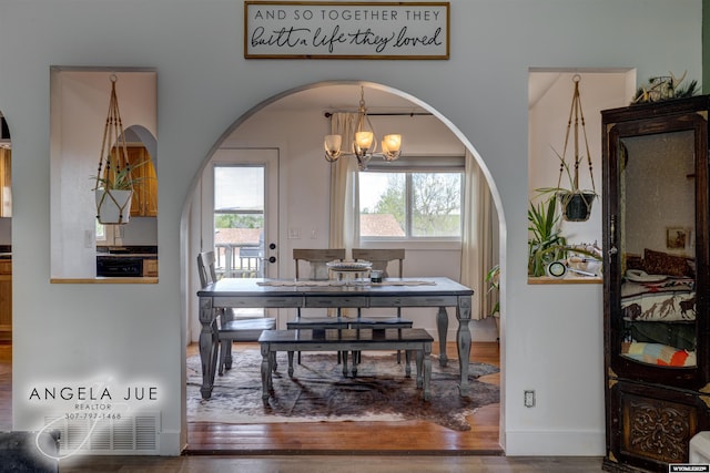 dining room featuring arched walkways, a chandelier, and wood finished floors