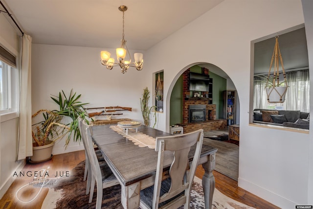 dining room with a chandelier, a brick fireplace, wood finished floors, and baseboards