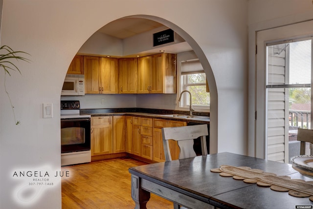 kitchen featuring range with electric stovetop, white microwave, a sink, dark countertops, and light wood-style flooring