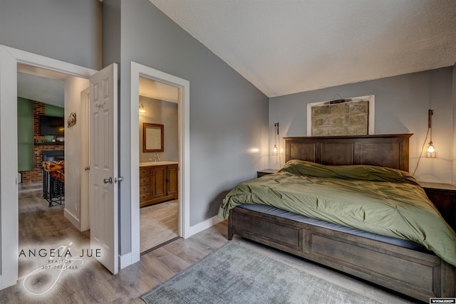 bedroom featuring wood finished floors, vaulted ceiling, a fireplace, connected bathroom, and baseboards