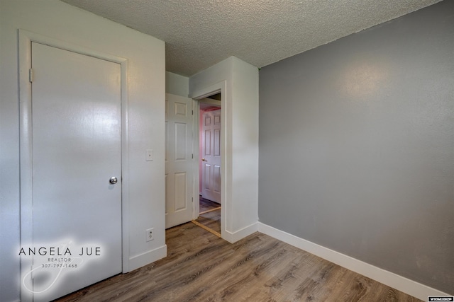 unfurnished bedroom featuring wood finished floors, baseboards, and a textured ceiling