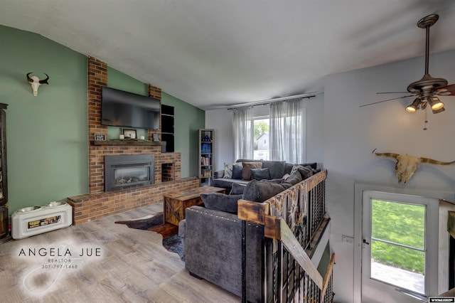 living area featuring a ceiling fan, wood finished floors, a brick fireplace, and vaulted ceiling