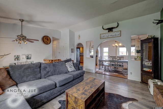 living room with arched walkways, wood finished floors, ceiling fan, vaulted ceiling, and a chandelier
