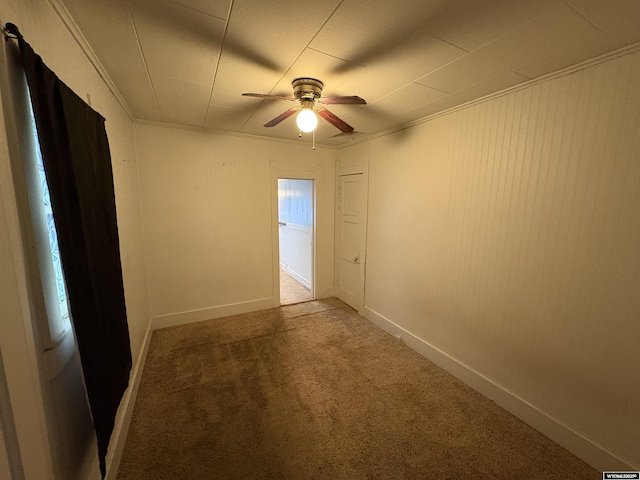 empty room with ceiling fan, carpet floors, crown molding, and baseboards