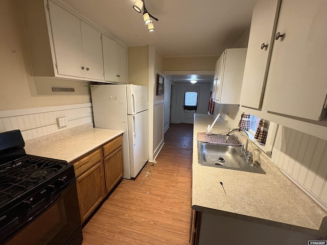 kitchen with black gas range, a sink, light wood-style flooring, freestanding refrigerator, and light countertops
