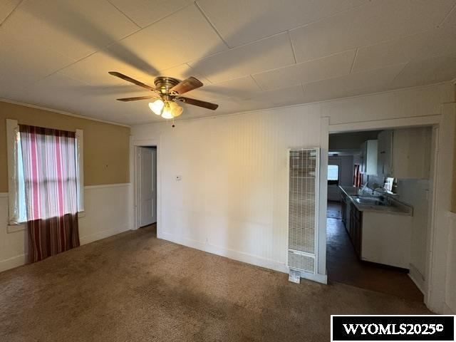 carpeted spare room featuring a heating unit, ceiling fan, and a sink