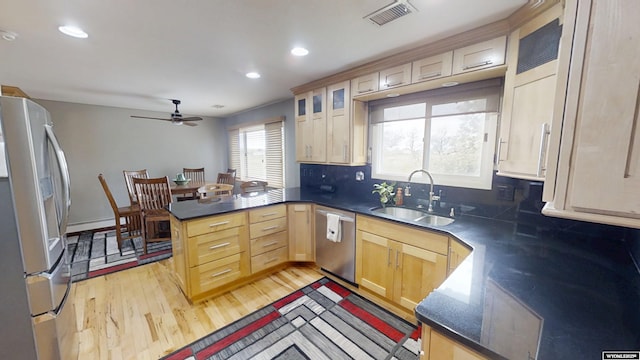 kitchen with stainless steel appliances, a sink, a peninsula, light brown cabinets, and light wood-style floors