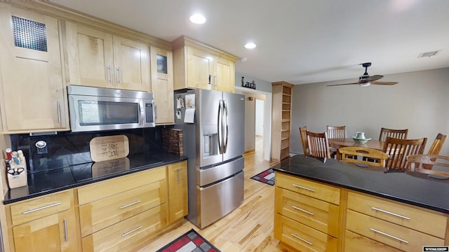 kitchen featuring appliances with stainless steel finishes, light wood finished floors, light brown cabinetry, dark countertops, and decorative backsplash
