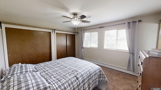 carpeted bedroom with multiple closets, a baseboard heating unit, a ceiling fan, and baseboards