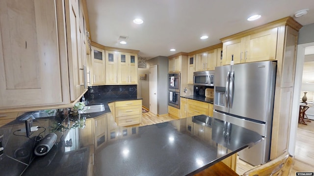 kitchen featuring appliances with stainless steel finishes, a peninsula, dark countertops, light brown cabinets, and recessed lighting