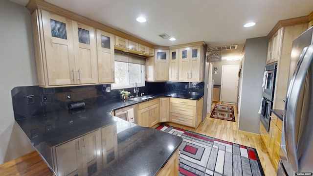 kitchen featuring light brown cabinets, a sink, light wood-style floors, stainless steel appliances, and backsplash