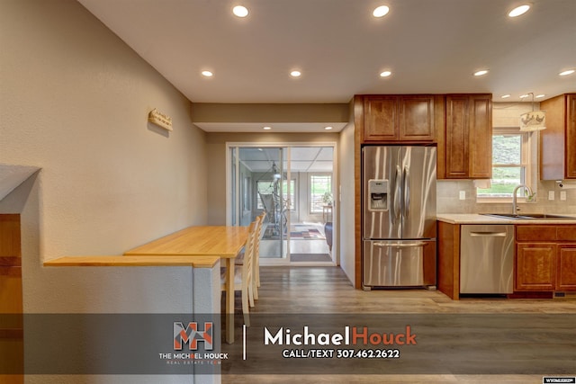 kitchen with appliances with stainless steel finishes, a sink, light wood-type flooring, brown cabinets, and recessed lighting