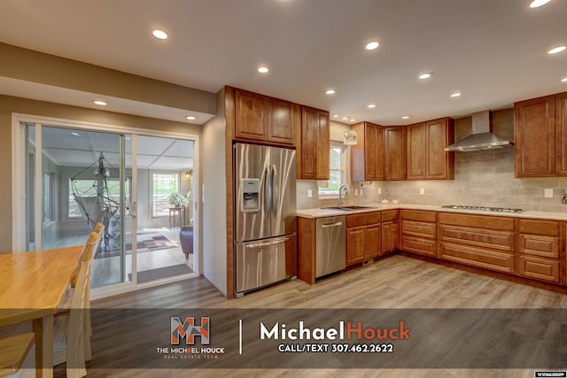 kitchen featuring appliances with stainless steel finishes, wall chimney exhaust hood, a sink, light wood-style flooring, and light countertops