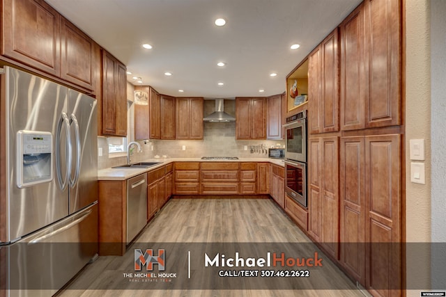 kitchen featuring appliances with stainless steel finishes, a sink, wall chimney range hood, light wood finished floors, and light countertops