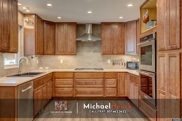 kitchen featuring a sink, wall chimney range hood, appliances with stainless steel finishes, brown cabinetry, and backsplash