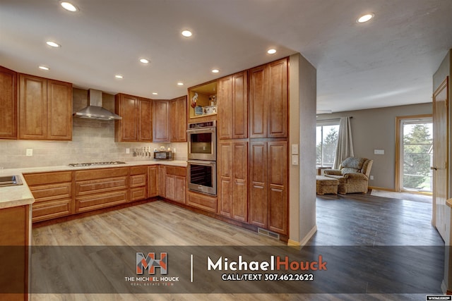 kitchen featuring wall chimney range hood, gas stovetop, double oven, light wood-type flooring, and recessed lighting