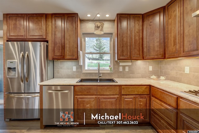 kitchen featuring appliances with stainless steel finishes, a sink, brown cabinets, backsplash, and recessed lighting
