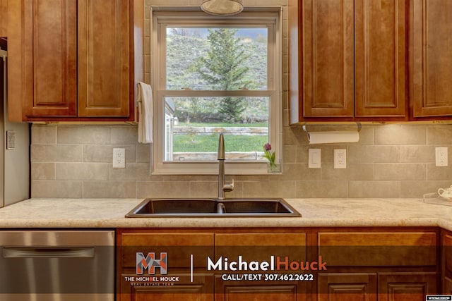 kitchen featuring stainless steel dishwasher, a sink, backsplash, and brown cabinetry