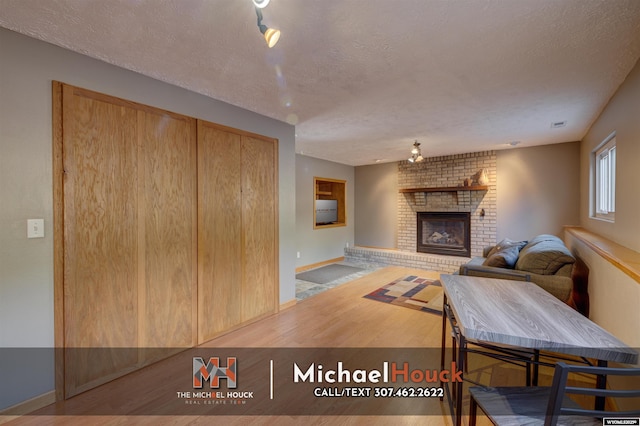 living area with a fireplace, a textured ceiling, baseboards, and wood finished floors