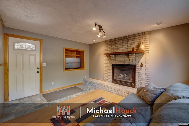 living area featuring a textured ceiling, wood finished floors, a fireplace, and baseboards
