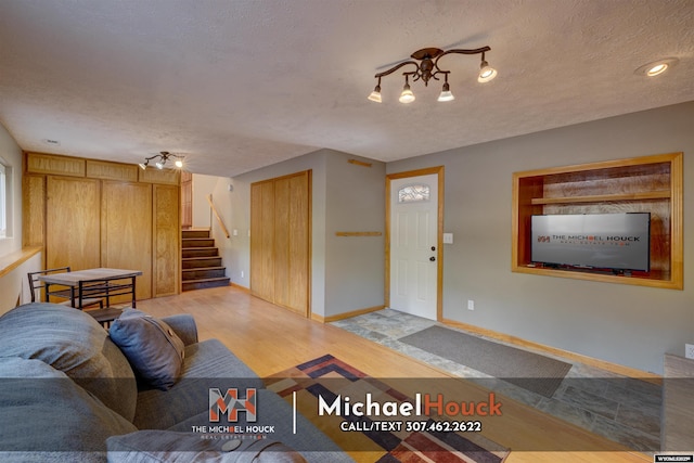 living area with stairs, wood finished floors, a textured ceiling, and baseboards