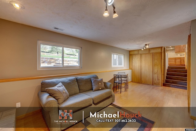 living area featuring light wood-style floors, a textured ceiling, stairs, and baseboards