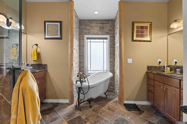 bathroom with baseboards, vanity, stone finish flooring, and a soaking tub