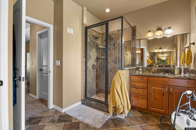 full bath with a stall shower, vanity, baseboards, and stone finish floors