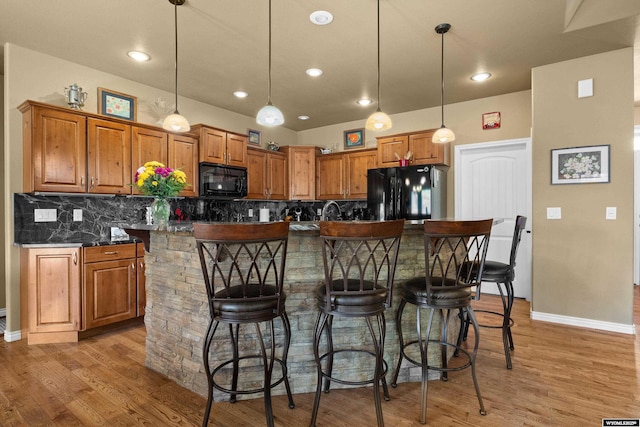 kitchen with black appliances, brown cabinetry, light wood-style flooring, backsplash, and recessed lighting