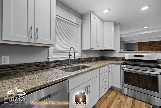kitchen with appliances with stainless steel finishes, a sink, light stone counters, white cabinetry, and recessed lighting