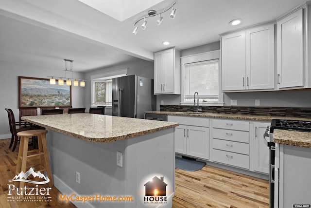 kitchen featuring stainless steel gas range, fridge with ice dispenser, a sink, a center island, and light wood-type flooring