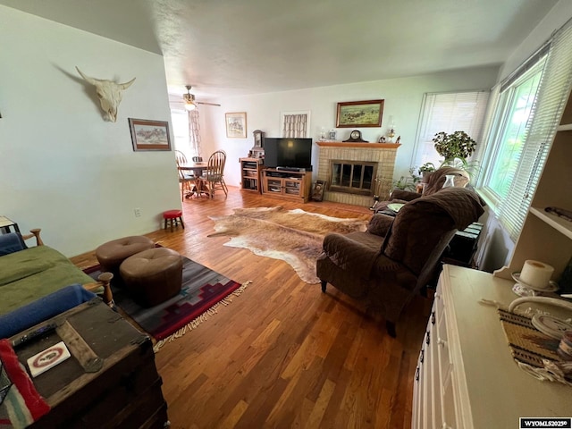 living area with wood finished floors, ceiling fan, and a brick fireplace