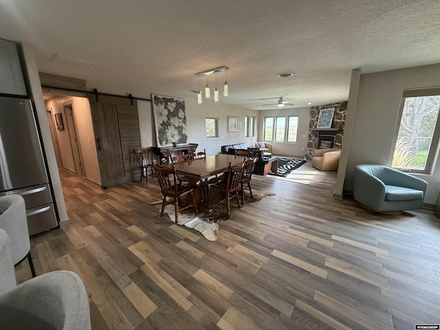 41 Ridgewater Ln, Douglas, WY 82633 - dining room featuring a barn door, wood finished floors, a stone fireplace, a textured ceiling, and ceiling fan