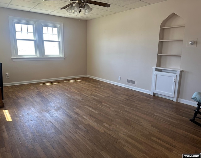 101 9th, Sinclair, WY 82334 - unfurnished living room with ceiling fan, dark wood-style floors, baseboards, a paneled ceiling, and built in shelves