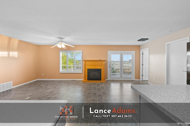 396 Williams Way, Glenrock, WY 82637 - unfurnished living room with plenty of natural light, a textured ceiling, a ceiling fan, a glass covered fireplace, and baseboards