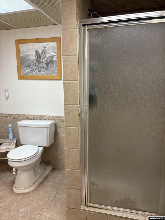 715 Emerald St, Kemmerer, WY 83101 - bathroom with tile walls, a shower stall, toilet, tile patterned flooring, and a wainscoted wall