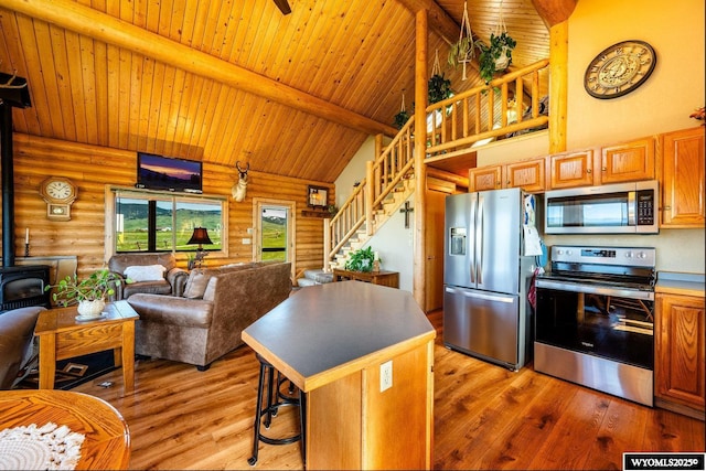 49 Cheyenne Rd, Banner, WY 82832 - kitchen featuring appliances with stainless steel finishes, a wood stove, rustic walls, wooden ceiling with exposed beams, and light wood-style floors