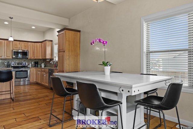 2511 Mercy Ln, Casper, WY 82609 - kitchen with stainless steel appliances, a kitchen breakfast bar, decorative backsplash, light wood finished floors, and decorative light fixtures