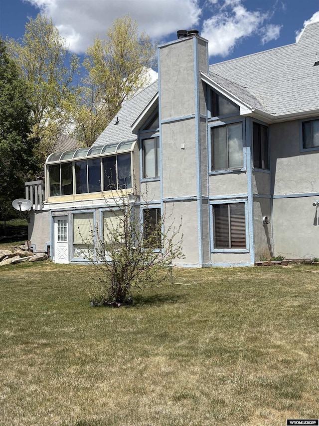 221 Rimrock Dr, Evanston, WY 82930 - back of property with a sunroom, a shingled roof, stucco siding, and a lawn