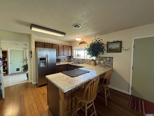 302 Clearview St, Saratoga, WY 82331 - kitchen featuring appliances with stainless steel finishes, a peninsula, light countertops, light wood finished floors, and a textured ceiling