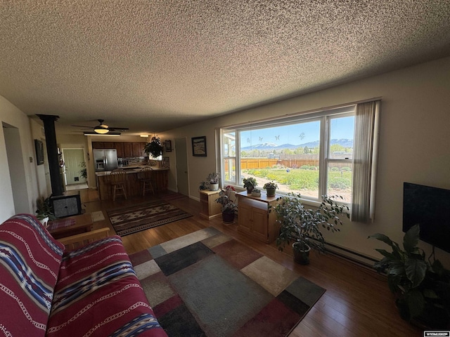 302 Clearview St, Saratoga, WY 82331 - living area with a textured ceiling, wood finished floors, a baseboard radiator, ceiling fan, and a wood stove