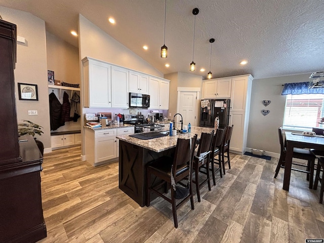 3440 Summit, Rock Springs, WY 82901 - kitchen featuring black appliances, a kitchen breakfast bar, a center island with sink, white cabinetry, and light stone countertops