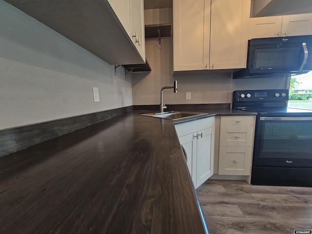 2502 E C St, Torrington, WY 82240 - kitchen with black appliances, a sink, wood finished floors, dark countertops, and white cabinetry