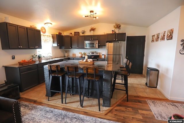 108 Tamari Dr, Buffalo, WY 82834 - kitchen featuring stainless steel appliances, a sink, a kitchen breakfast bar, light wood-style flooring, and vaulted ceiling