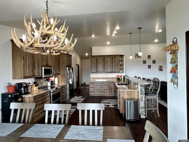 207 Eagle Dr, Greybull, WY 82426 - kitchen featuring appliances with stainless steel finishes, a sink, a chandelier, a kitchen bar, and dark wood-style floors